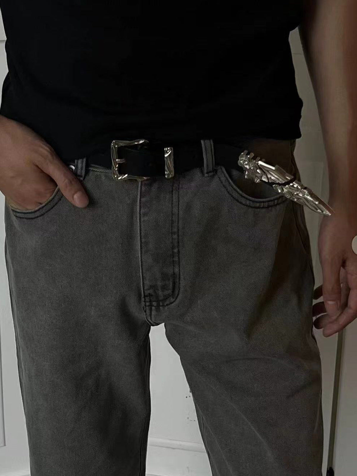 Cinturón negro con hebilla y punta plateadas grabadas – en modelo, con jeans grises | XoKool